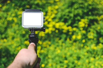 Action camera mockup in a man's hand. Against the background of yellow daisies in the garden.