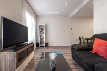 Living room with black velvet sofa, flat TV on a cabinet in front and wooden floors