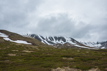 Dramatic alpine landscape with snowy mountains in gray low clouds. Bleak atmospheric scenery of...