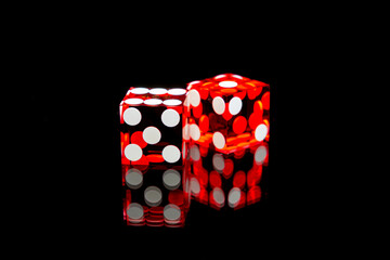Professional casino-style dice on a reflective surface isolated against a black background. 