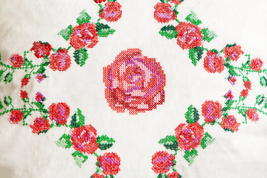 Decorative element, cross-stitch embroidery of rose flowers, on white linen fabric.