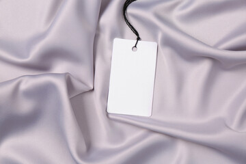 Blank tag on silver silky fabric, top view. Space for text