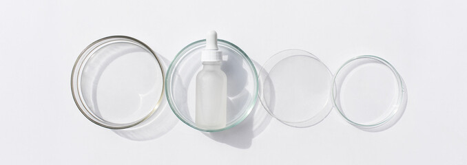 Banner Glass bottle in petri dish on white background. Top view, flat lay. Concept skincare. Dermatology science cosmetic laboratory. Natural medicine, cosmetic research, organic skin care products.