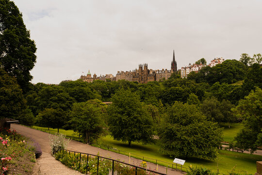 Photo of Edinburgh Old town between the foliage of the trees grown in Princess Street garden during a cloudy summer day