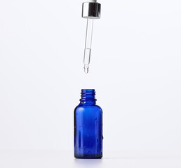 essential oil falling from the amber glass dropper. Blue bottle of cosmetic oil with a pipette