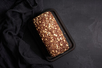 baked square rye flour bread with oatmeal on black background, top view