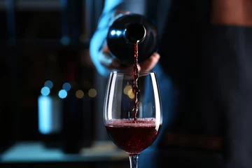 Poster Bartender pouring red wine from bottle into glass indoors, closeup © New Africa