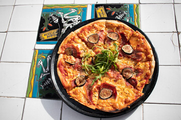 Pizza de higo con jamón serrano y arúgula sobre mesa de mosaicos 