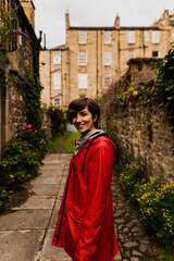 Young female posing with a red raincoat in the middle of a close during a rainy summer day in Edinburgh.