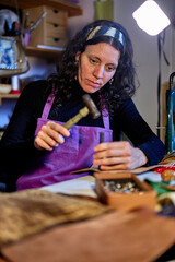 Fototapeta premium Craftswoman hammering leather at the work table in her studio