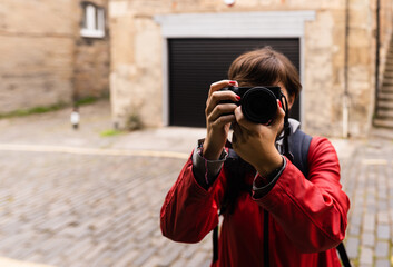 Attractive young female with a red raincoat and smiling while using a mirrorless camera