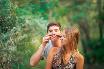 A guy and a girl are having fun in nature. A guy makes a mustache out of a girl's long hair.
