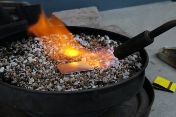 Annealing a piece of sterling silver metal with propane torch flame in a jewelry workshop.