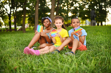 Fototapeta na wymiar children of different races sit on the grass and play with an anti-stress toy pop-it