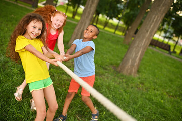 a group of children compete in a tug of war in the open air against the background of grass and park.