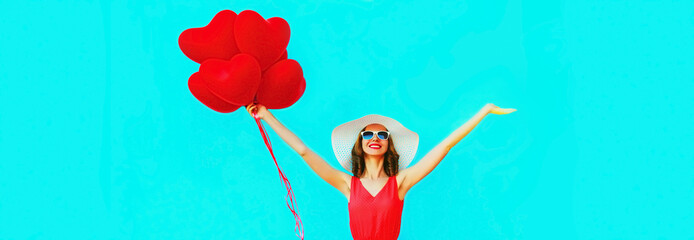 Beautiful happy smiling young woman with bunch of red heart shaped balloons wearing sunglasses on blue background