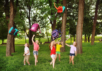 group of school children rejoice at the beginning of the summer holidays, throw up their school...