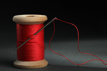 Red sewing thread with needle on black background, closeup