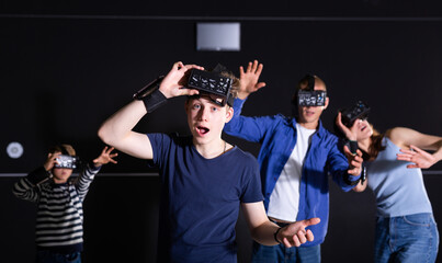 Portrait of emotional surprised teenage boy wearing VR headset playing virtual reality games with his parents and little brother