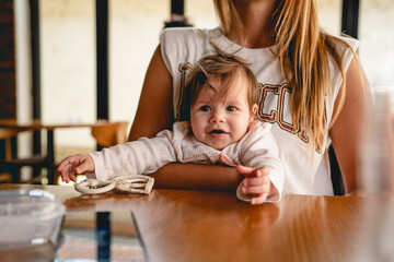 Small caucasian baby infant daughter in hands of her mother sitting by the table at restaurant...
