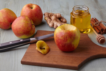 Apple prepared for baking in the oven surrounded by ingredients with honey, cinnamon and ginger