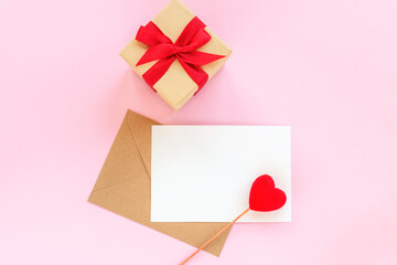 Blank paper and envelope with red heart and gift box on pink background, top view, flat lay, mockup. Valentines day concept, 14 february