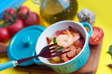 Baked shrimps with tomatoes, garlic, lemon, olive oil and mint in blue bowls on a yellow background. Shrimp on fork