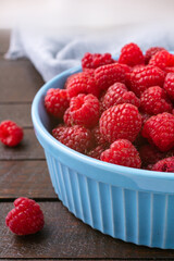 Red raspberry berry in plate on wooden table.