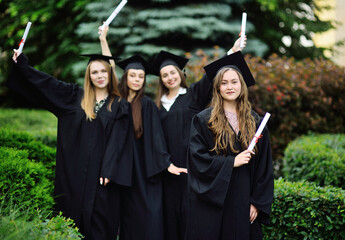pretty young girl is a college graduate student in a black robe smiling holding a diploma in her...