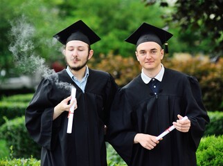 oung male graduate student in a black robe and a square hat smokes his diploma or certificate....