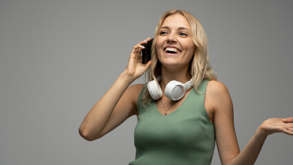 Closeup photo of attractive positive laughing young blonde woman communicating on mobile phone and smiling isolated on grey background.