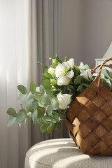 Stylish wicker basket with bouquet of flowers on ottoman in room