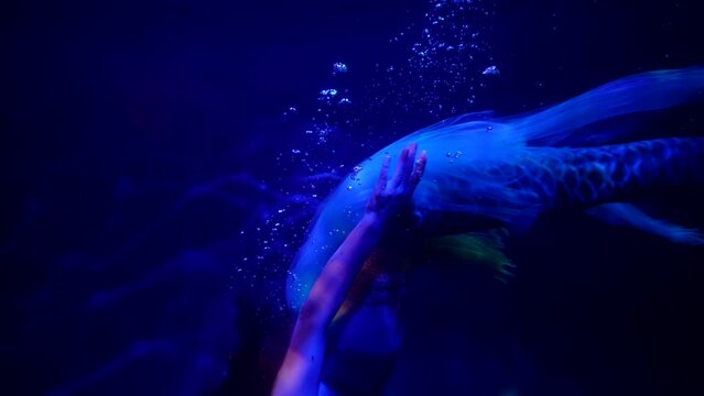 stunning underwater shot with swimming mermaid in dark blue depth, graceful woman with fish tail