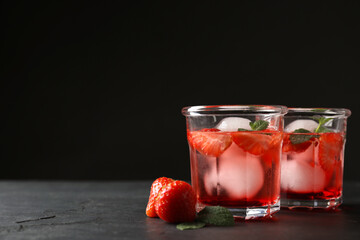 Delicious cocktails with strawberries, mint and ice balls on black table, space for text