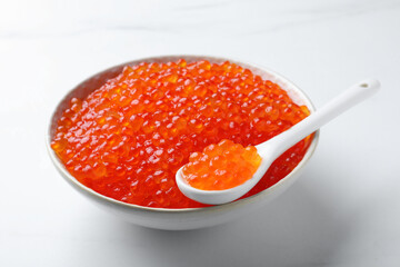 Bowl and spoon with delicious red caviar on white table
