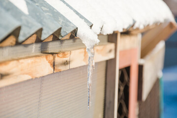 The icicle is melting. Water drips from the roof. Winter is retreating. The ice is melting. Seasons. Low temperature.