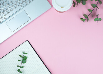 flat lay of notebook, laptop, take away cup and green leaves on pink background 