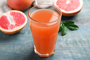 Tasty freshly made grapefruit juice on blue wooden table, closeup