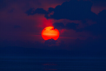 The red sun hid behind the clouds during a bright sunset.