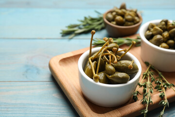Tasty capers, thyme and rosemary on light blue wooden table, space for text