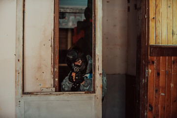 Photo of paintball player in goggle mask and camouflage aiming by paintball gun. Selective focus