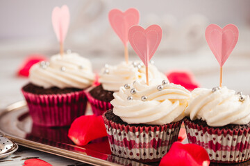 Buttercream cupcakes decorated with silver candies and paper hearts close-up. Soft focus.