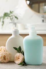 Fototapeta na wymiar Dispensers of liquid soap and roses on light grey table in bathroom