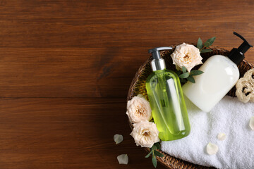 Dispensers of liquid soap, towel and roses in wicker basket on wooden table, top view. Space for text