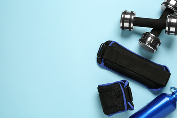 Weighting agents, dumbbells and sport bottle on light blue background, flat lay. Space for text