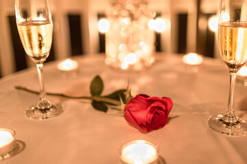 Single red rose on and champagne on restaurant table. Romantic candle light Valentines Day dinner.