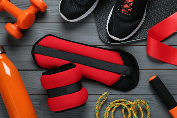 Red weighting agents and sport equipment on grey wooden table, flat lay