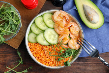 Delicious lentil bowl with shrimps and cucumber on wooden table, flat lay