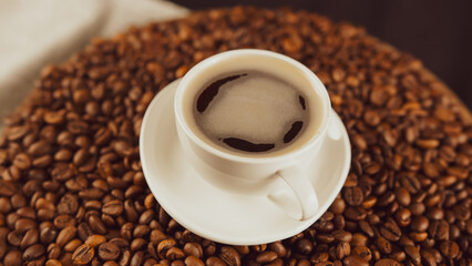 Cup of coffee and saucer on coffee beans. Composition of freshly brewed coffee on roasted beans. Concept of preparation fragrant drink.