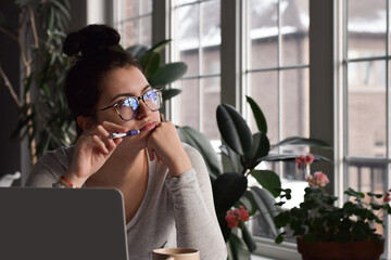 Young girl student in glasses sitting at desk in deep thought